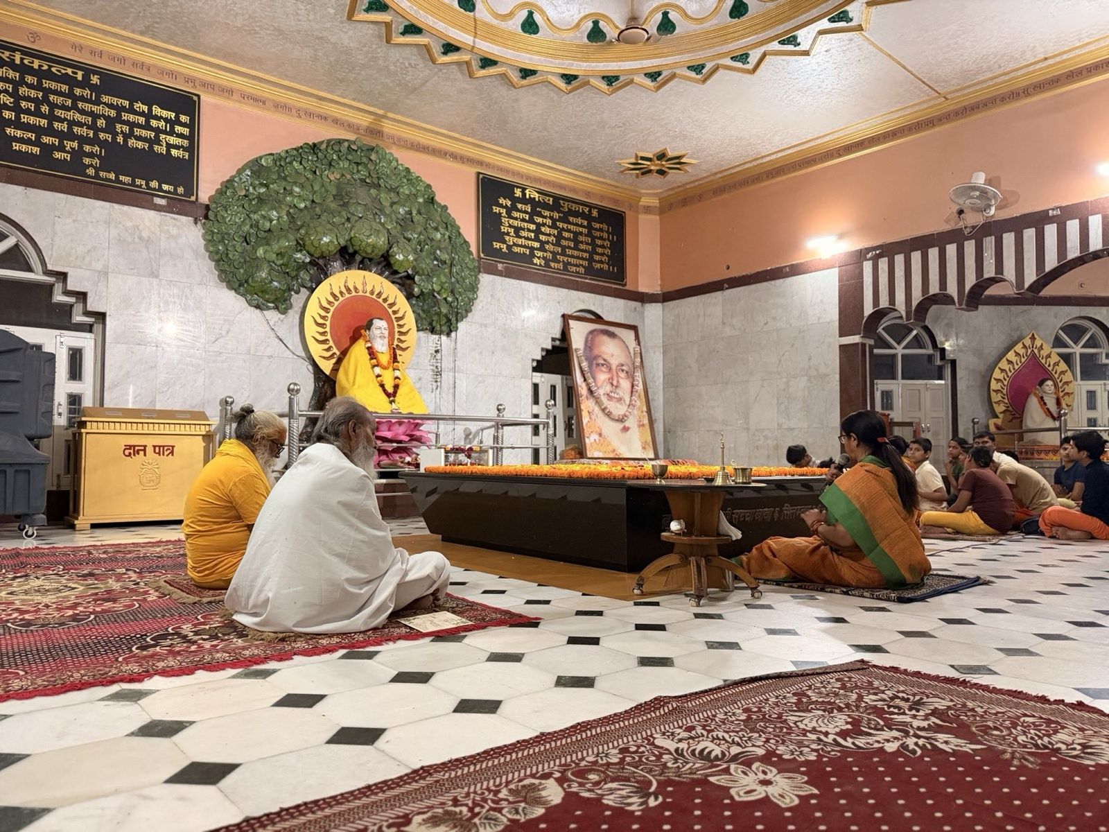 Guests and priests seated in prayer in a marble-floored temple hall
